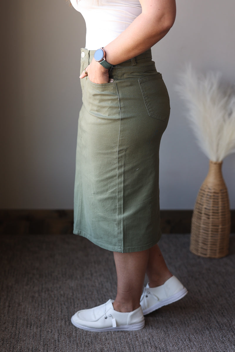 Person wearing a green skirt and white sneakers in a minimal indoor setting