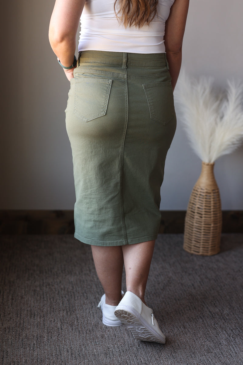 Person wearing a green skirt and white sneakers in a room with a textured wall and decorative vase.