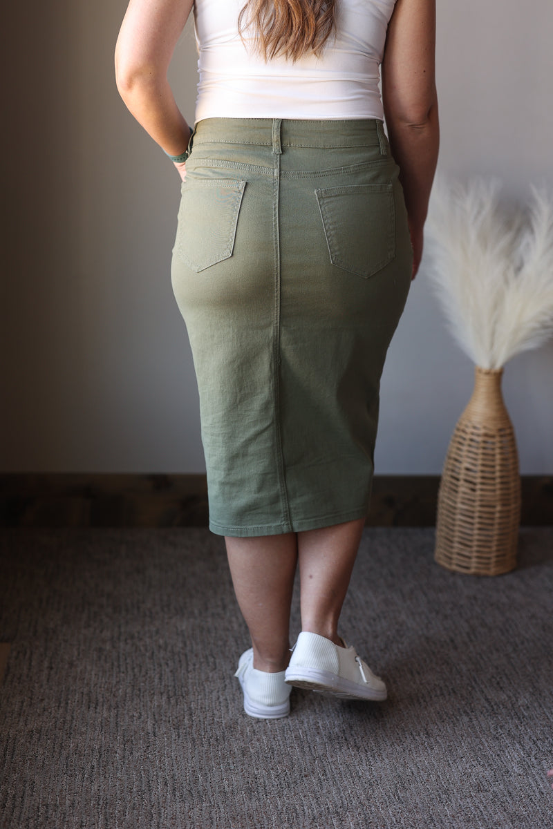 Person wearing a green skirt standing in a room with a textured wall and decorative item.