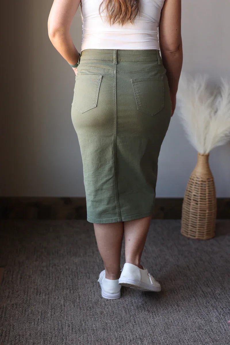 Person wearing a green skirt standing in a room with a textured wall and decorative item.