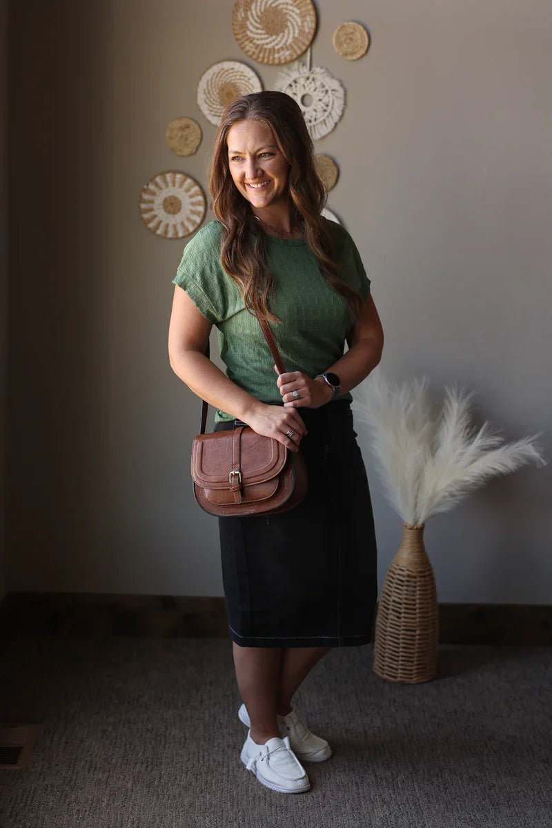 Woman holding a brown leather bag in a room with decorative wall art and plants.