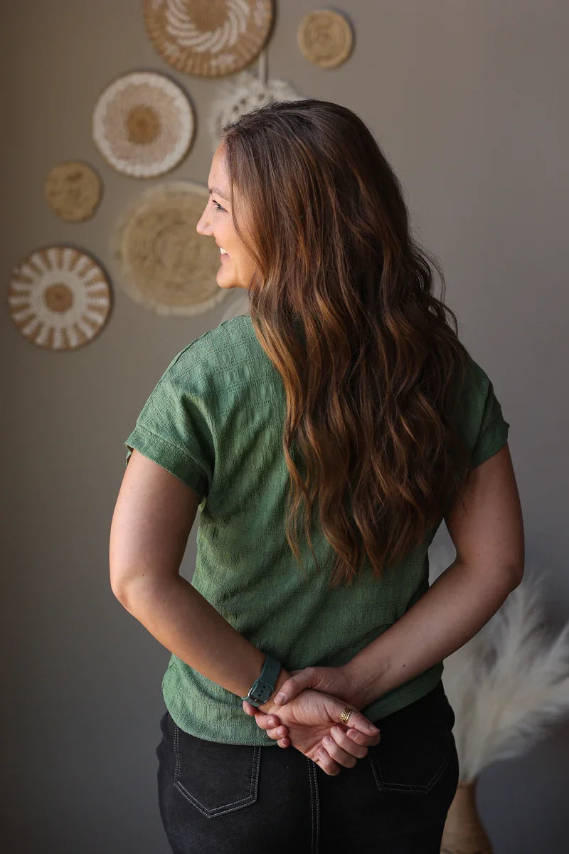 Woman in a green shirt holding hands with another person against a wall with decorative plates.