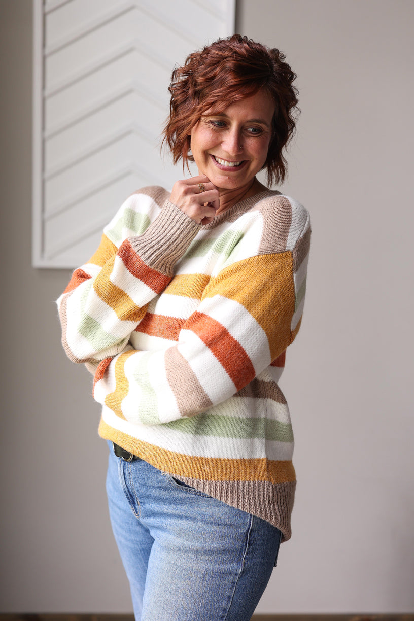 Woman wearing a colorful striped sweater and blue jeans indoors.