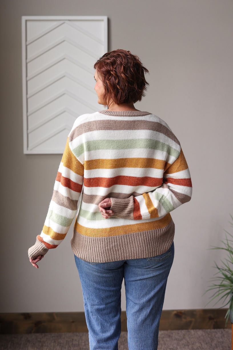 Person wearing a striped sweater and blue jeans standing in a room with a plant and framed picture on the wall.