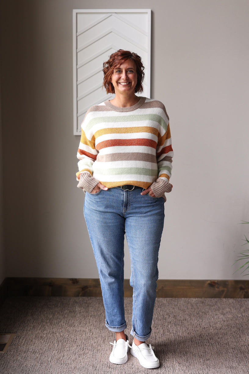 Person wearing a striped sweater and jeans standing indoors.