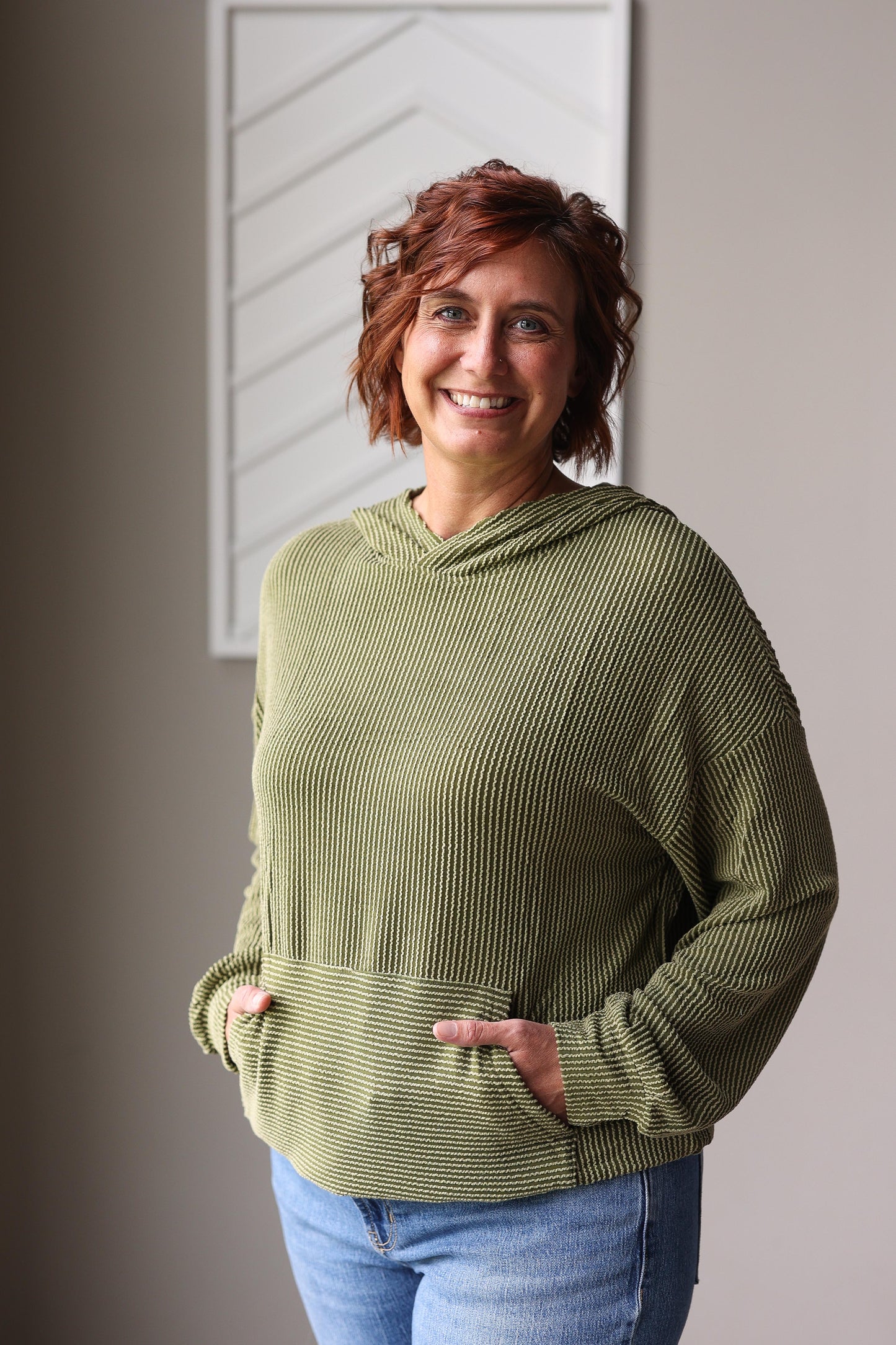Woman wearing a green textured sweater standing indoors against a neutral wall.