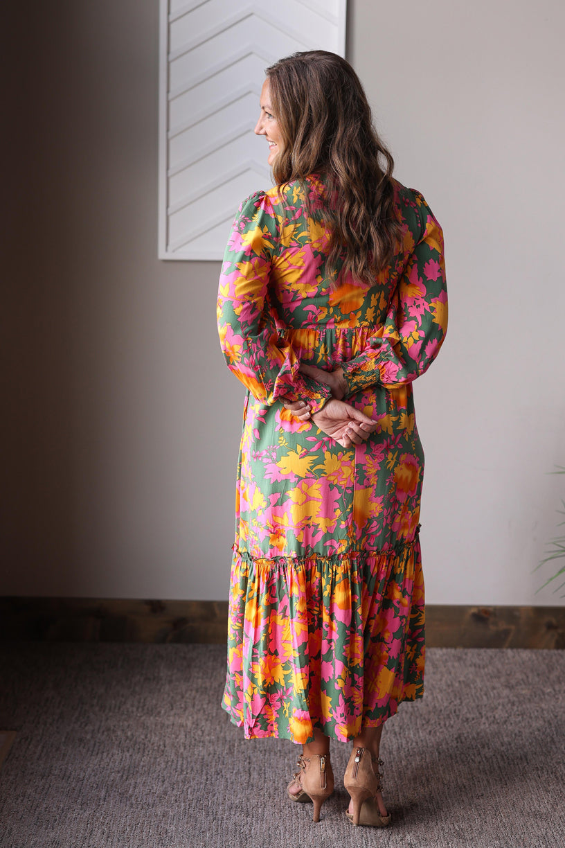 Woman wearing a colorful floral dress standing in a room with a neutral background.