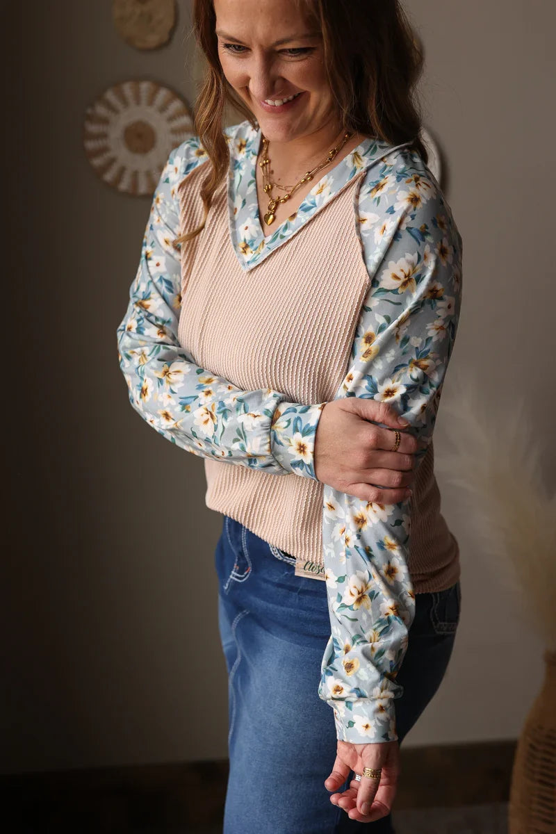 Woman wearing a floral long-sleeve top over a beige sweater and blue jean skirt indoors.