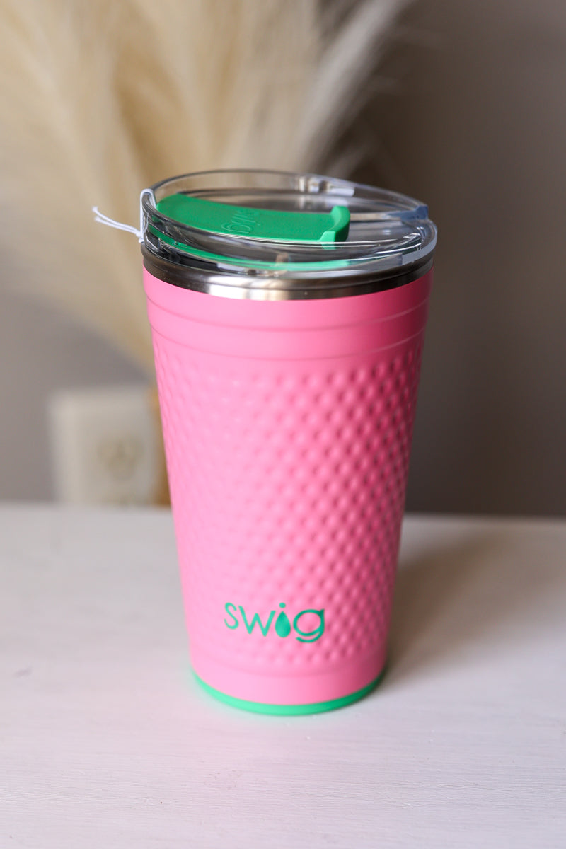 Pink swig tumbler with a green lid on a pink golf dimple surface SWIG