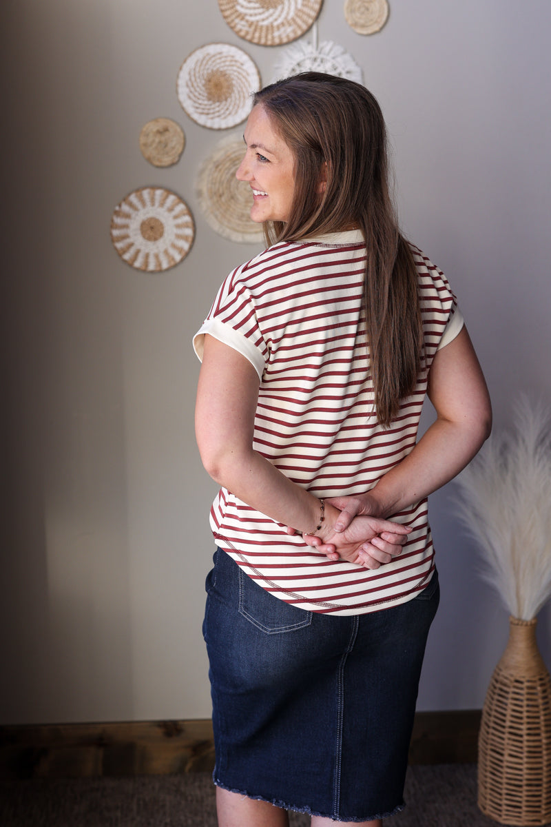 Woman wearing a striped shirt and denim skirt standing in a room with decorative wall art.