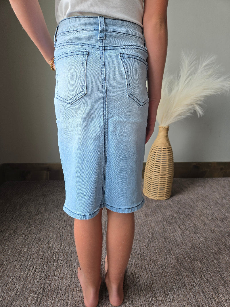 A person wearing light-wash denim shorts, shown from the back in a home setting with a woven vase on a neutral surface.