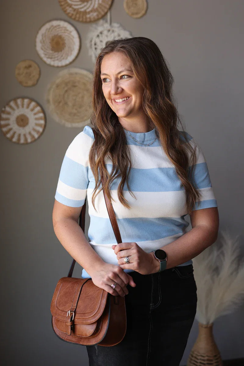 Woman wearing a striped shirt with a brown bag, standing against a wall with decorative plates.