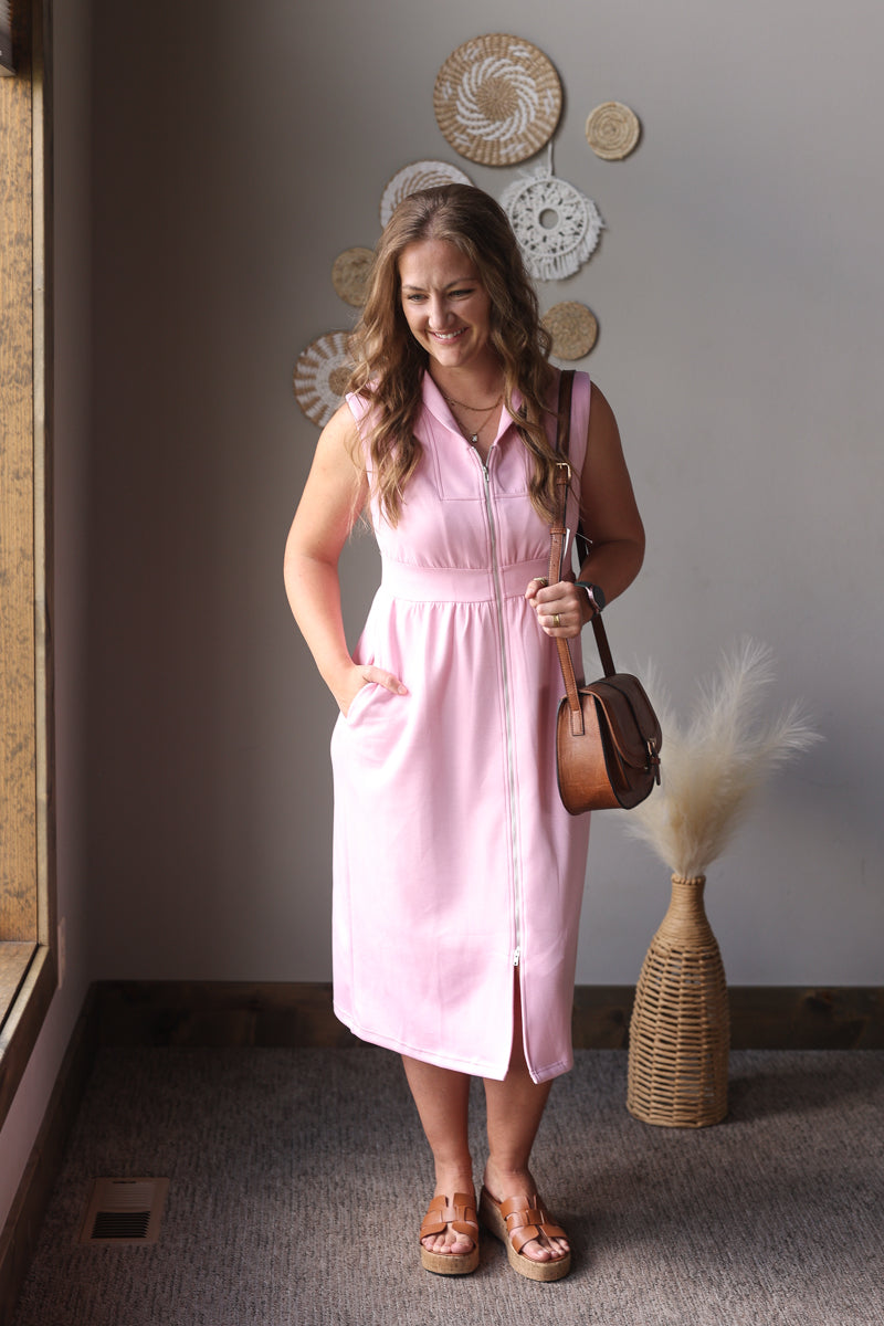 Woman in a pink dress standing in a room with decorative wall art and a vase.