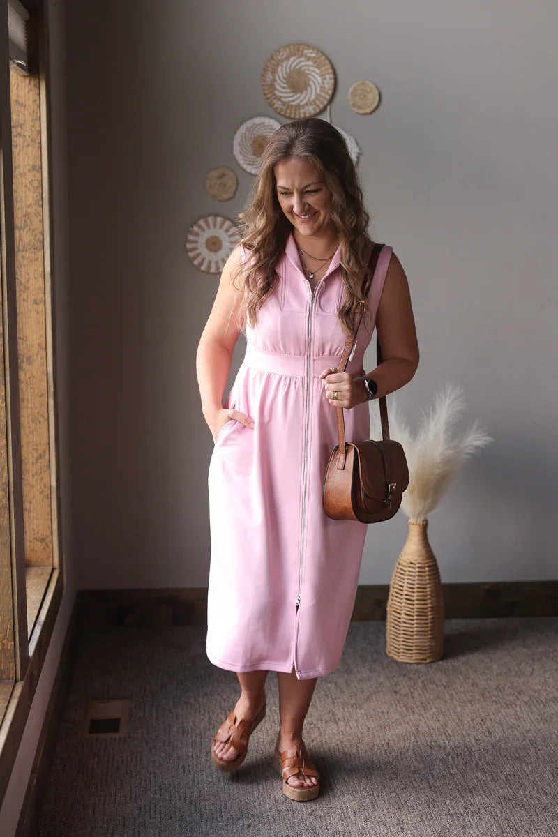 Woman in a pink dress standing in a room with decorative elements on the wall.