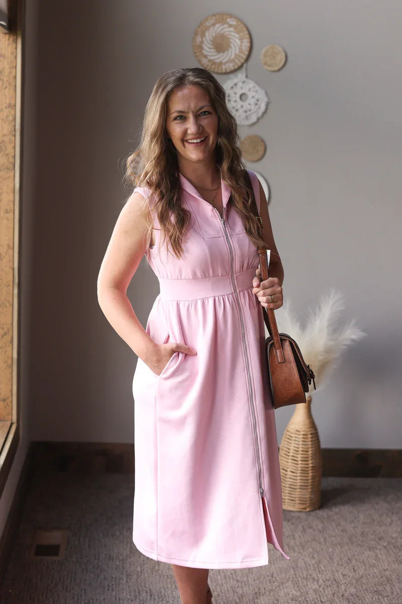 Woman in a pink dress standing indoors with decorative elements on the wall.
