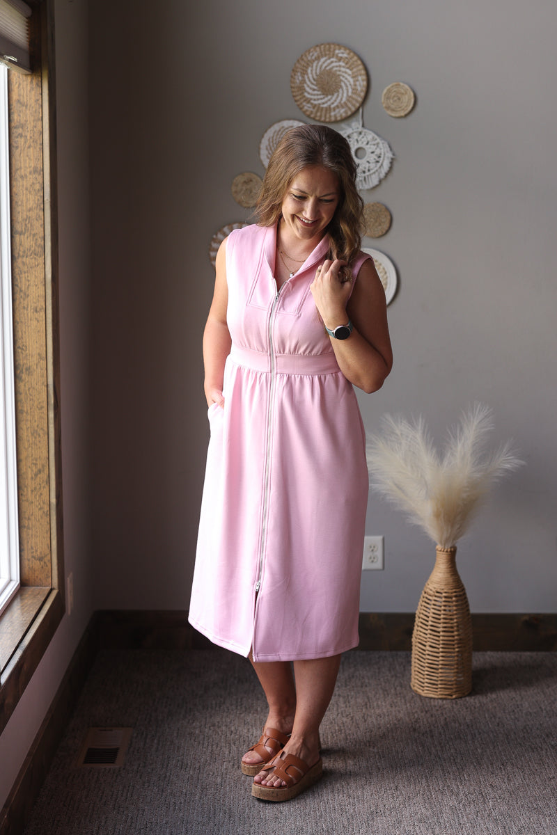 Woman in a pink dress standing in a room with decorative plates on the wall.