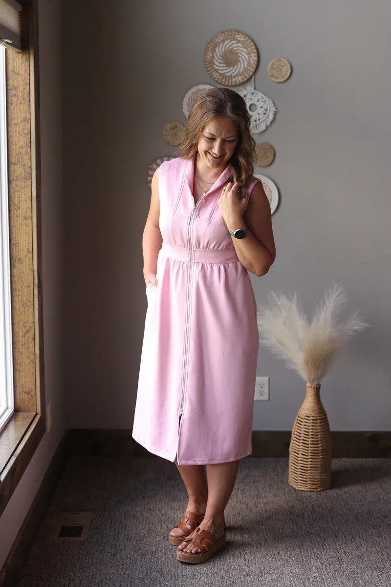 Woman in a pink dress standing in a room with decorative plates on the wall.