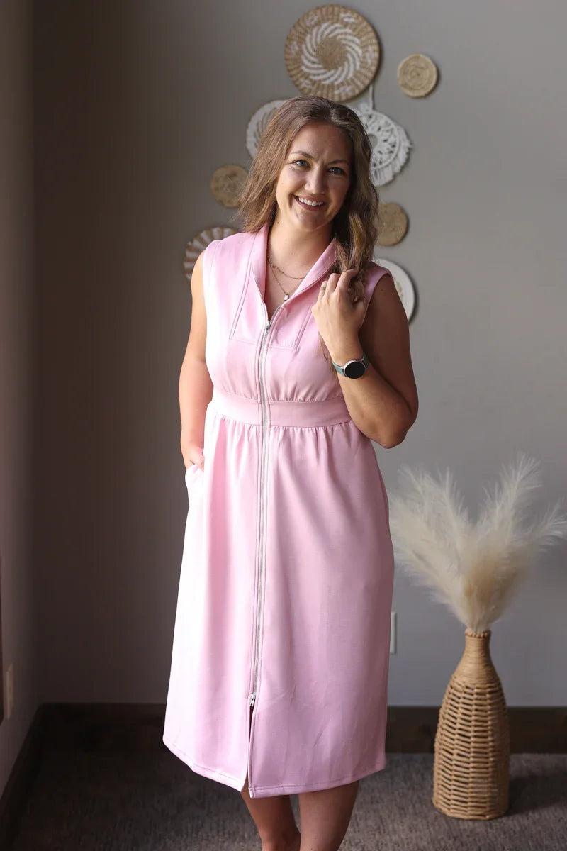 Woman wearing a pink dress standing in a room with decorative wall art and a vase.