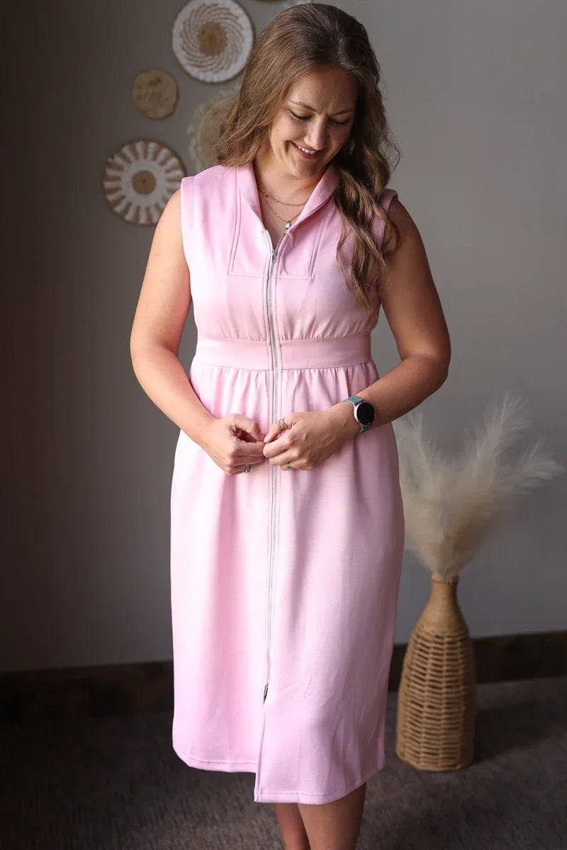 Woman wearing a pink dress standing against a neutral wall with decorative elements.