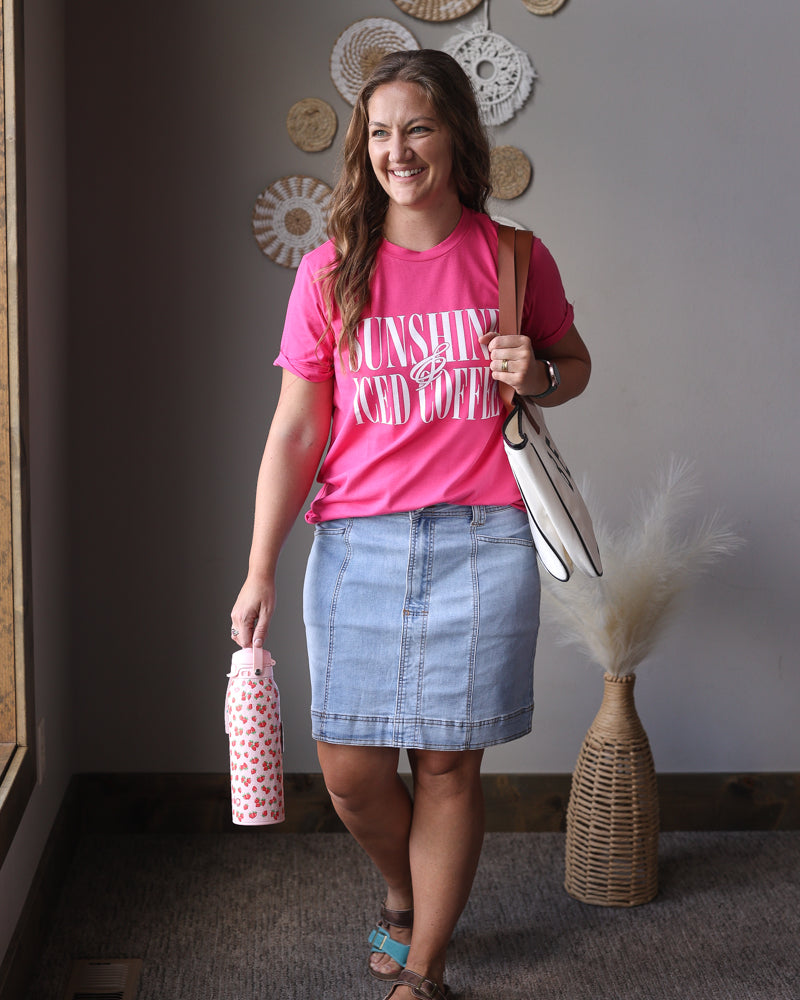 Woman in pink shirt and denim skirt standing indoors with decorative wall art in the background