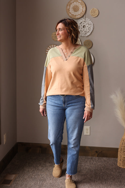 Woman wearing a colorblock vneck top and blue jeans standing in a room with decorative wall hangings for a cute easy fall winter outfit.