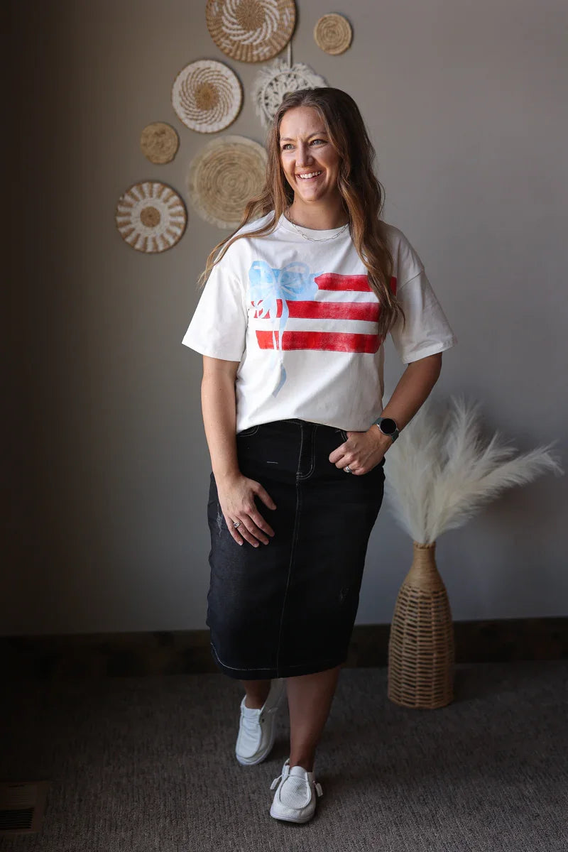 Woman wearing a white t-shirt with a colorful graphic design, standing in a room with decorative wall art.