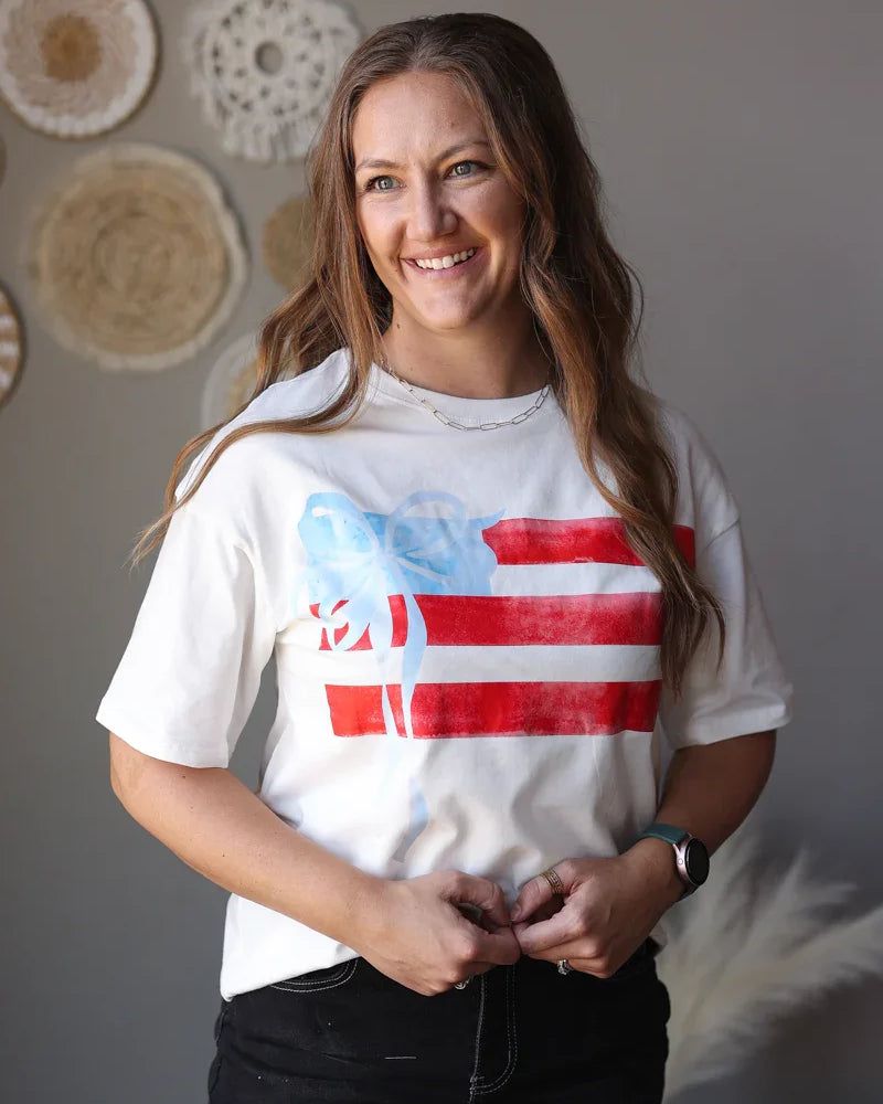 Woman wearing a white t-shirt with a graphic design, standing against a neutral wall.