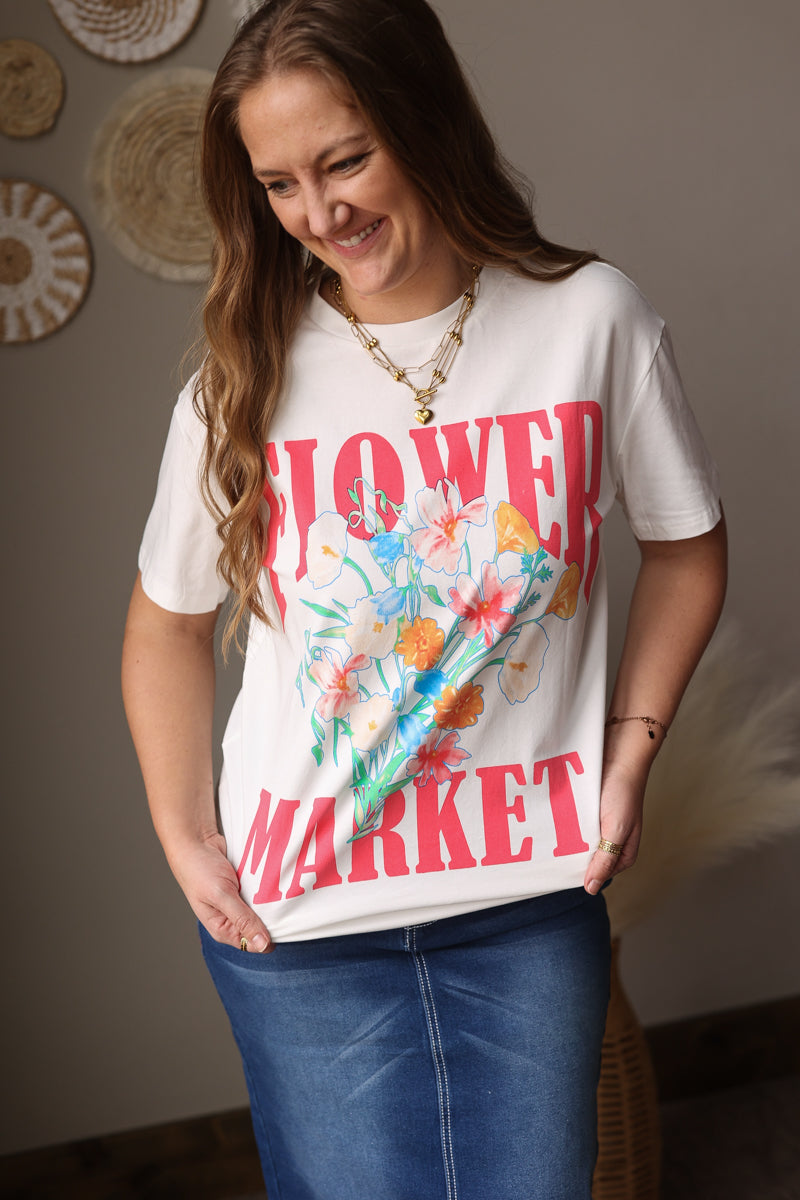 Woman wearing a white t-shirt with floral design and text, standing indoors.