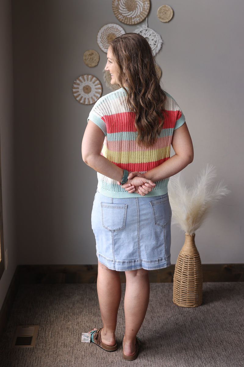 Woman wearing a colorful striped shirt and denim skirt standing in a room with decorative elements.
