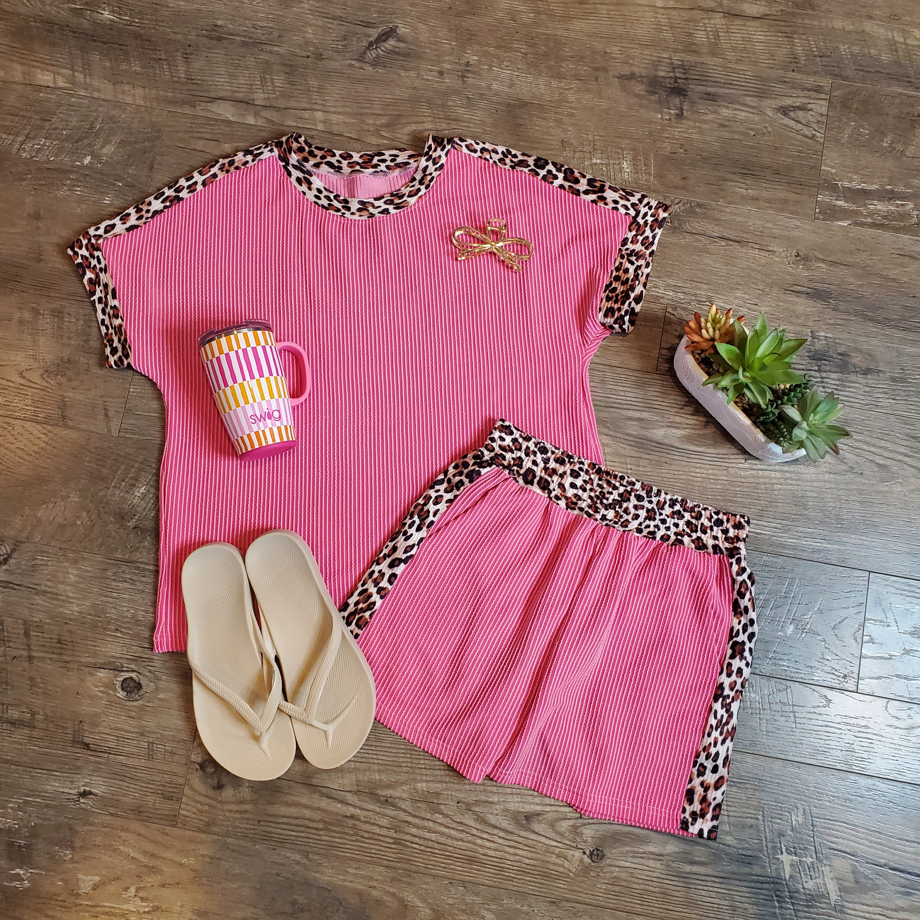 Pink outfit with leopard print trim, flip-flops, and a mug on a wooden floor.