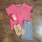 Pink top with leopard print sleeves, blue shorts, beige sandals, and a small bag on a wooden floor.