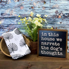 A styled home decor scene on a rustic wooden surface with a blue distressed wood plank backdrop. On the left, a folded white cloth napkin or towel with a black palm frond pattern sits in a woven basket.