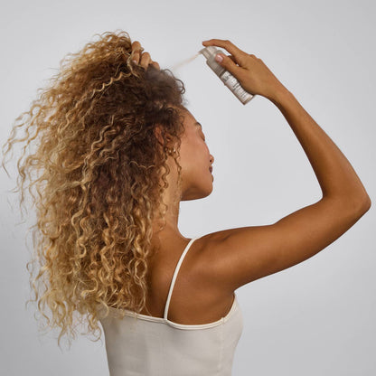 Woman applying hair product to her curly hair against a plain background