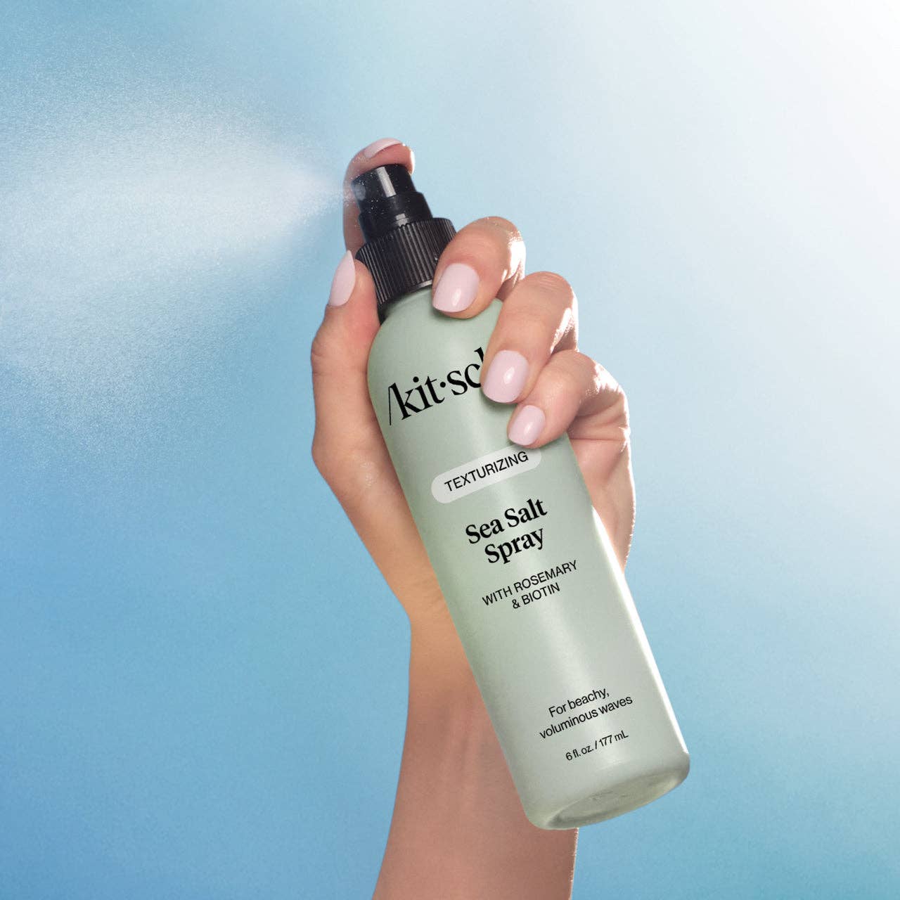 Hand holding a bottle of Kit-Sal Sea Salt Spray against a blue gradient background
