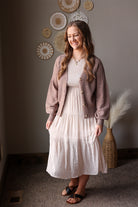 Woman wearing a light brown cardigan over a beige dress, standing in a room with decorative wall art.