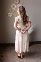 Woman in a beige dress standing in a room with decorative wall art.