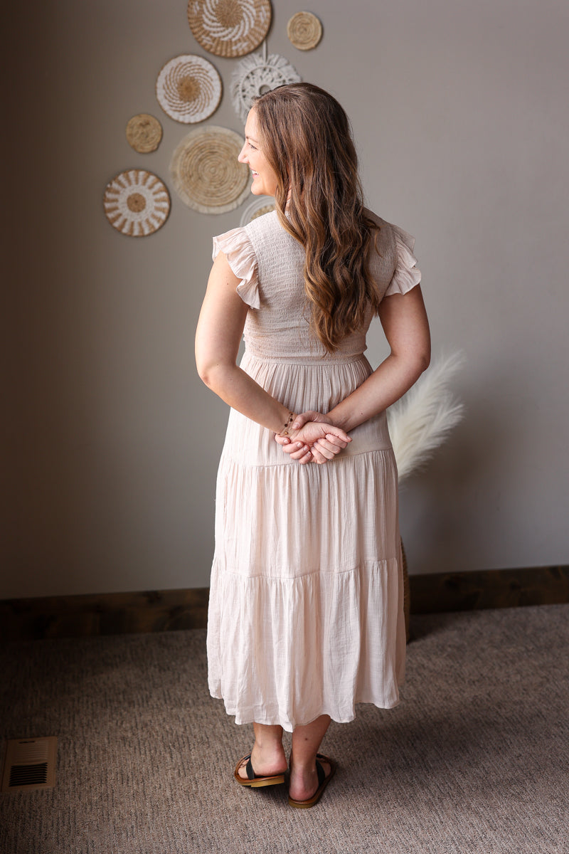 Woman in a beige dress standing in a room with decorative wall art.