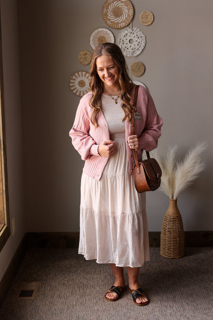 Woman in a pink cardigan and white dress standing in a room with decorative wall art.