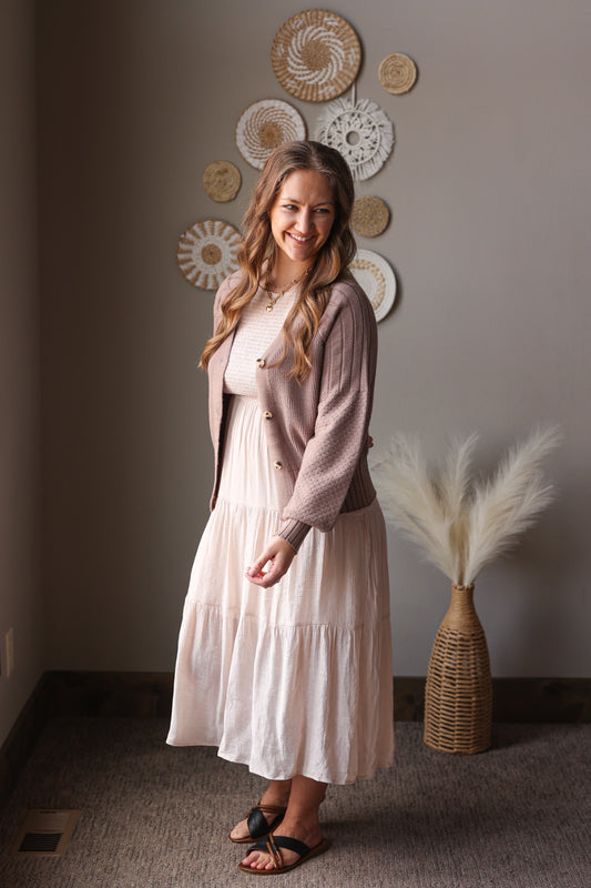 Woman in a light pink dress and cardigan standing in a room with decorative plates on the wall.