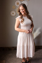 Woman wearing a tan dress standing in a room with decorative wall art.