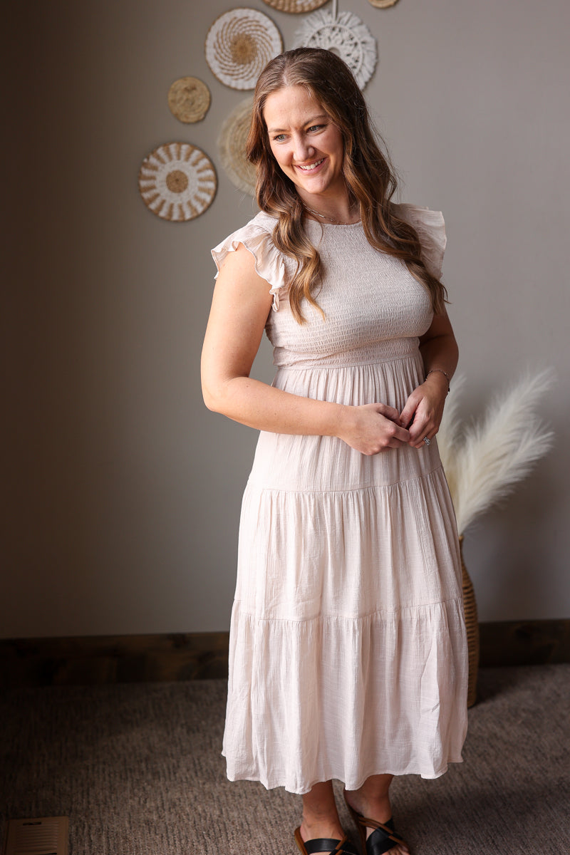 Woman wearing a tan dress standing in a room with decorative wall art.