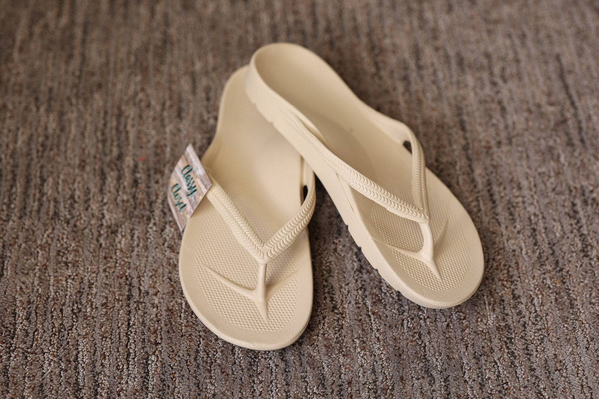Pair of beige flip-flops on a textured brown surface