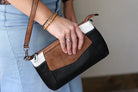 Person holding a black and brown handbag with light blue jeans and a patterned top.