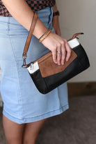 Person holding a black and brown clutch bag with denim skirt and sandals.