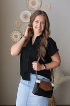 Woman wearing a black button up blouse, holding a black handbag with a brown interior, standing against a wall with decorative plates.