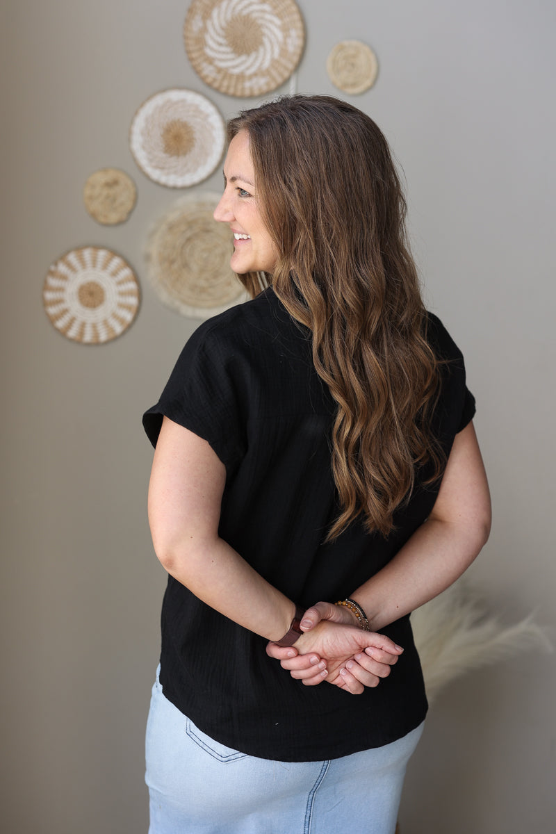 Woman wearing a black shirt and light blue jean skirt standing against a wall with decorative circular patterns.