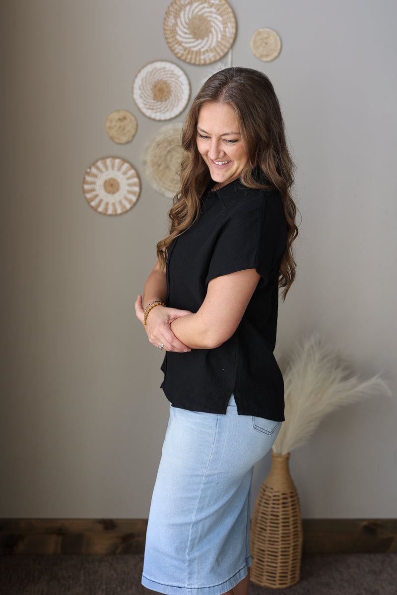 Woman in black top and light blue jean skirt standing in a room with decorative wall art.