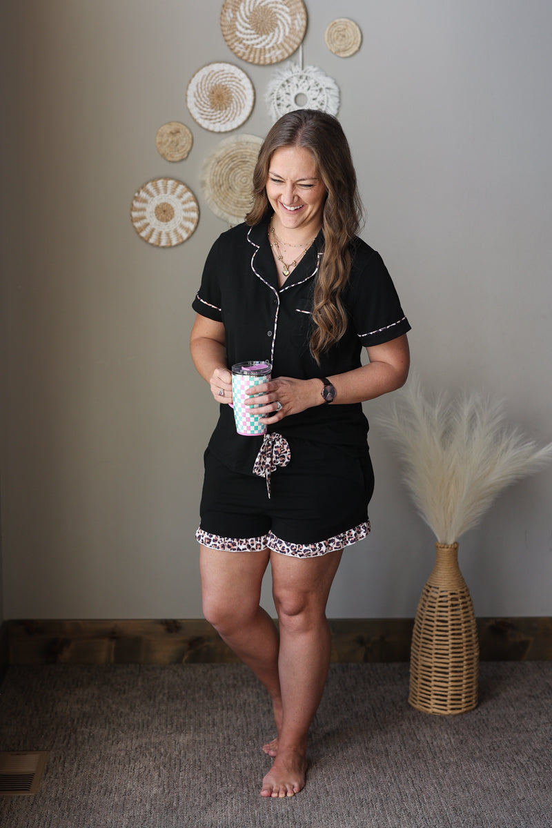 woman wearing a black 2 piece button up shorts pajama lounge set with animal leopard trim contrast