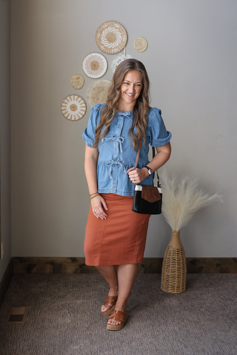 Woman in a blue top and rust skirt standing in a room with decorative wall art.