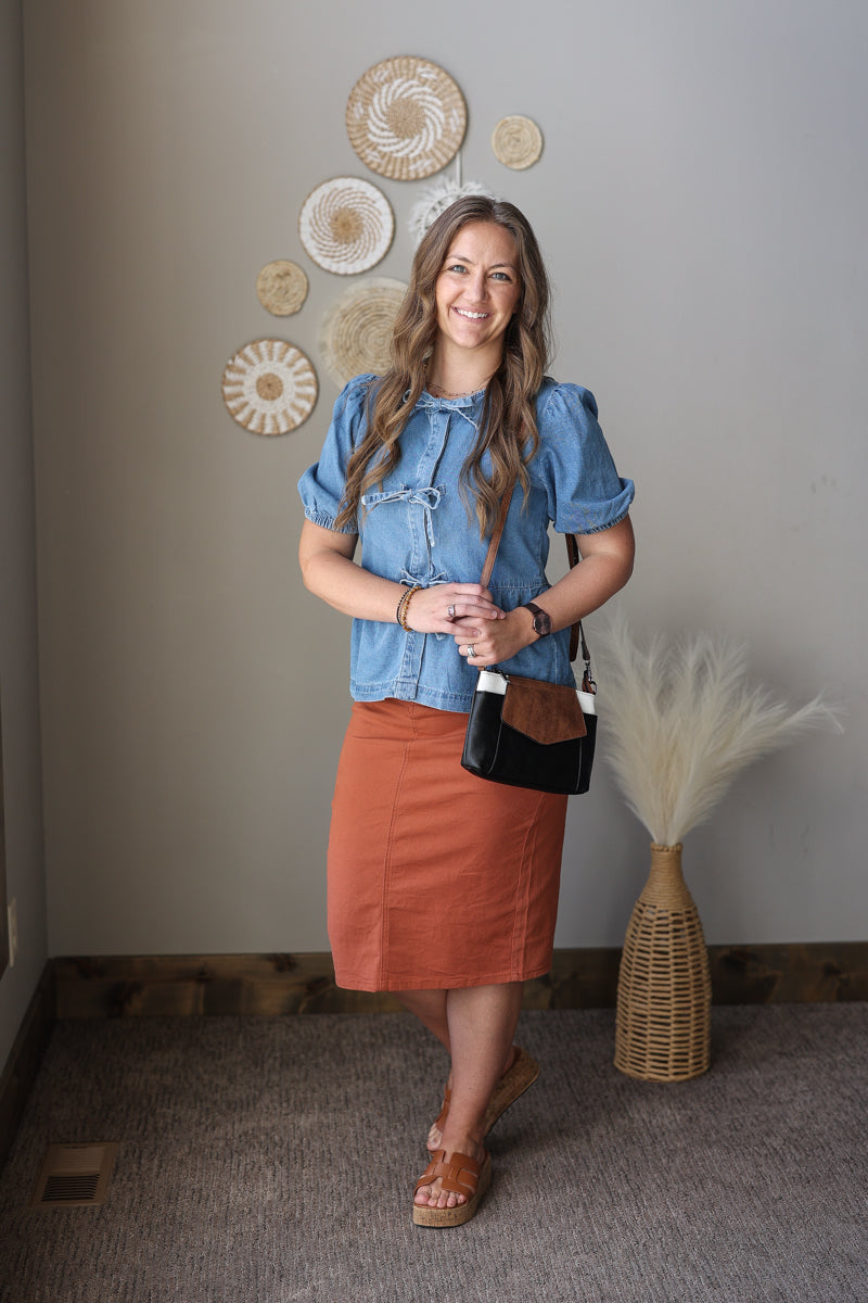 Woman in a blue top and orange skirt standing in a room with decorative wall art.